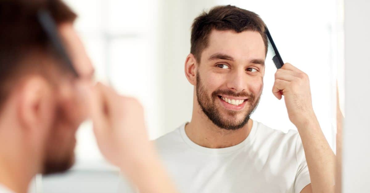 Hombre peinando su cabello con un peine de dientes anchos frente al espejo, mostrando un peinado suave recomendado tras un injerto capilar