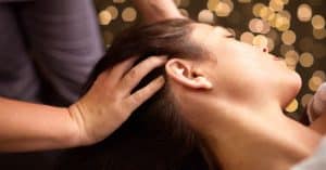 Manos realizando un masaje capilar en el cuero cabelludo de una mujer para estimular la circulación y relajar la zona.