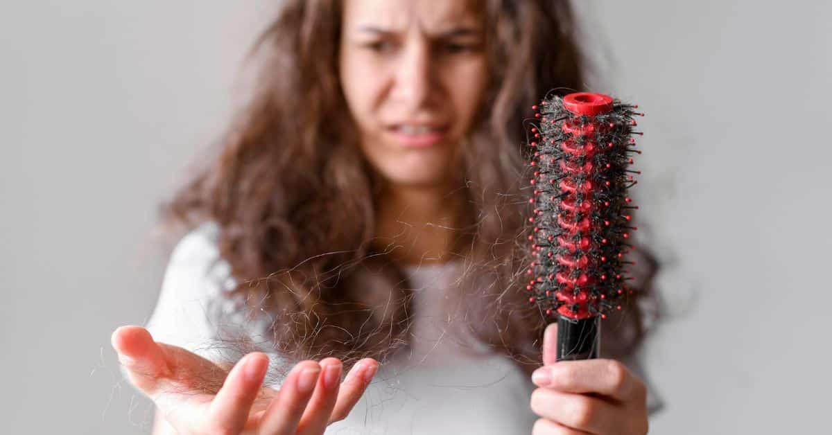 Mujer preocupada al ver mechones de cabello en un cepillo, una imagen que refleja la duda entre pérdida de cabello temporal o permanente.