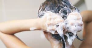 Persona lavando su cabello con abundante espuma, representando el impacto de los productos químicos en el cabello.