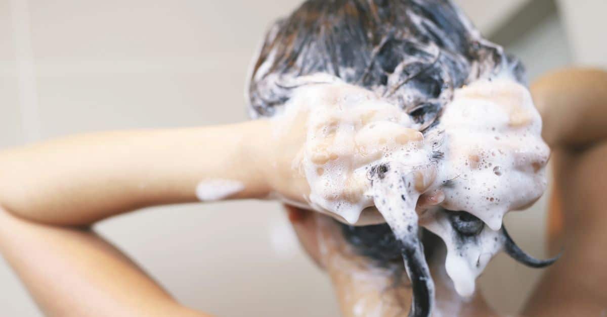 Persona lavando su cabello con abundante espuma, representando el impacto de los productos químicos en el cabello.